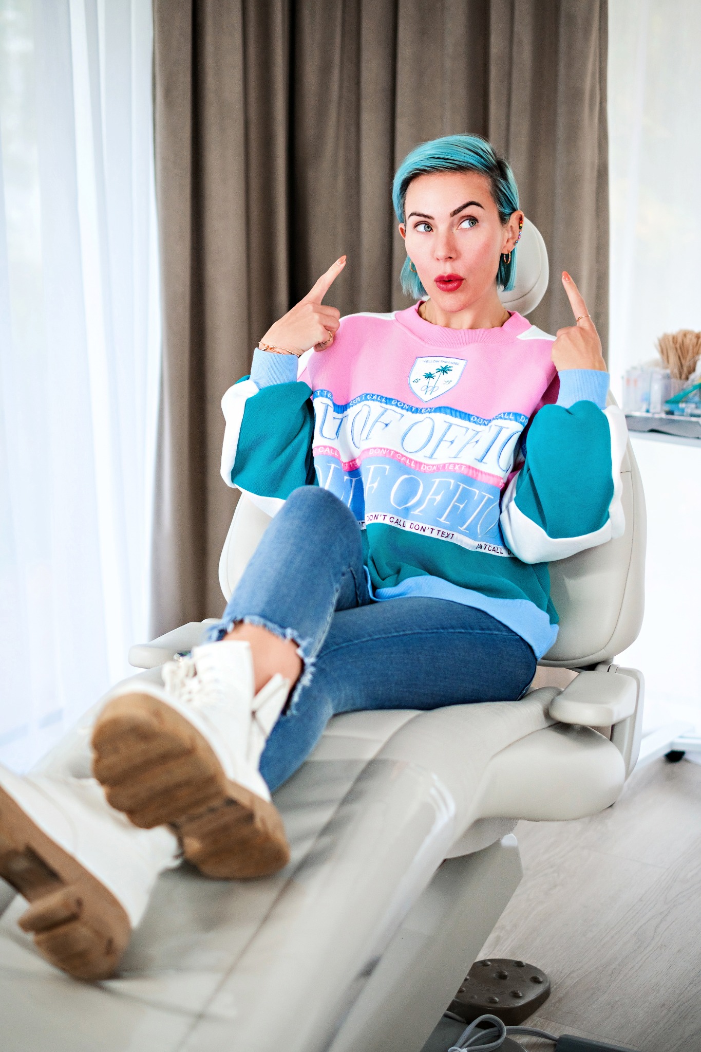 Chelsea seated in the treatment chair, smiling and gesturing playfully toward her face