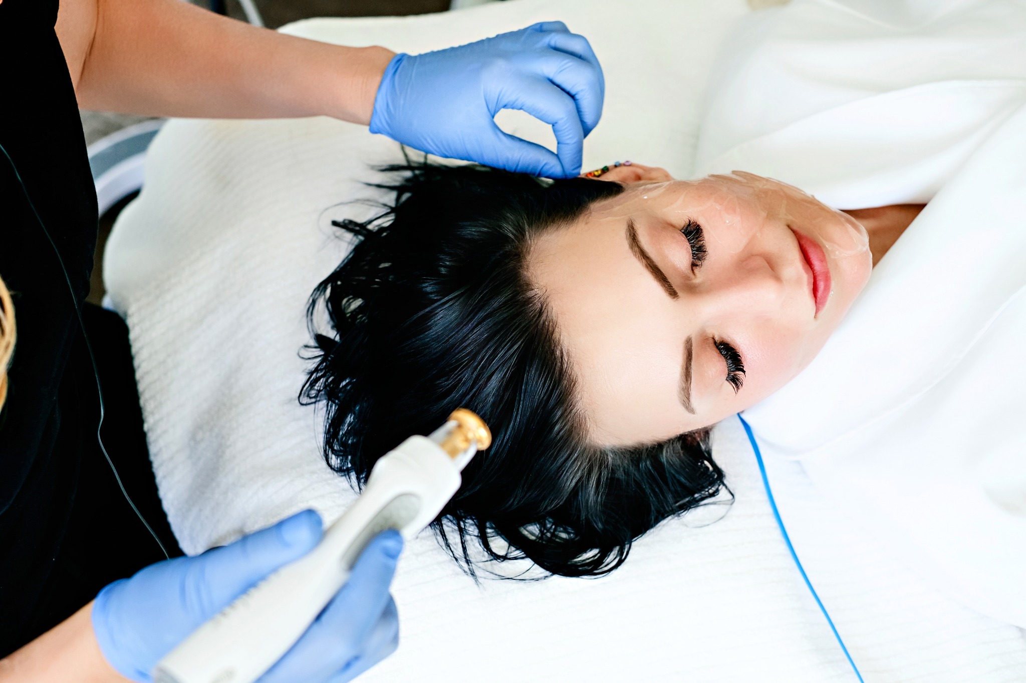 Provider in blue gloves treating a reclining patient's face with a professional device