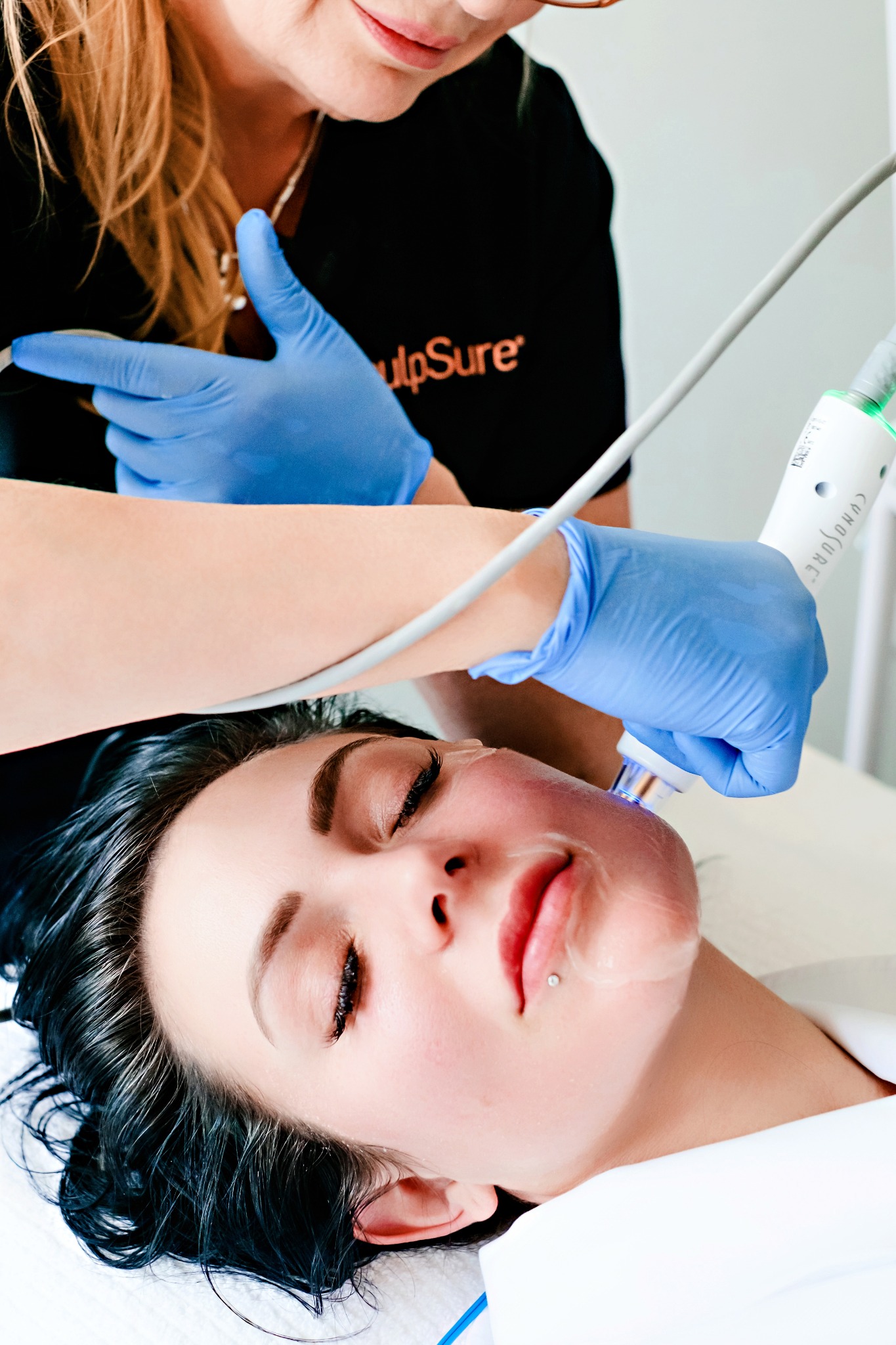 Provider guiding a facial treatment device across a patient's cheek during a clinical session