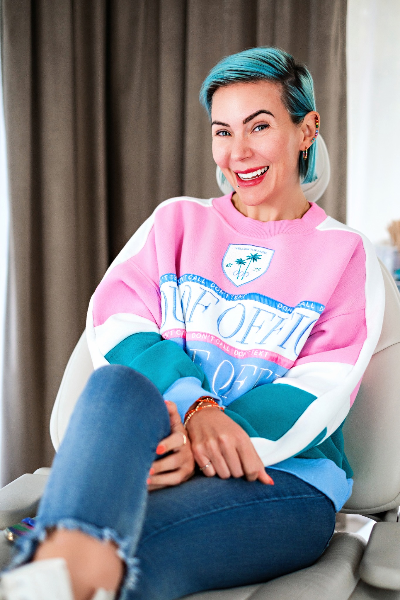 Chelsea Patricia smiling in a treatment chair wearing a pink, teal and blue colorblock sweatshirt